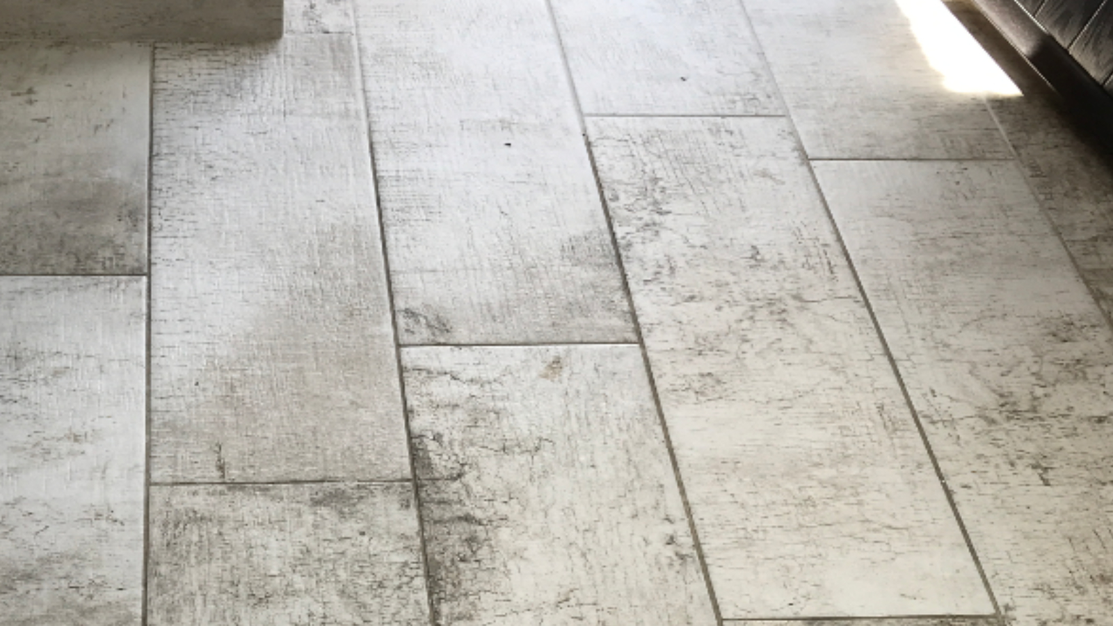 Driftwood-effect ceramic floor with discoloured white grout before professional cleaning